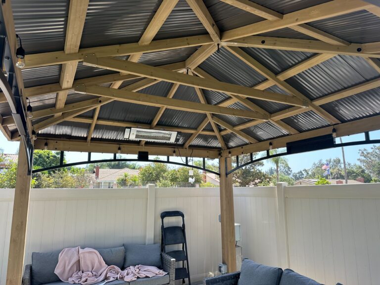 Finished timber pergola with corrugated metal roofing and exposed truss framing installed over a backyard patio. The...