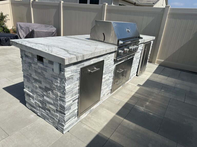Completed outdoor kitchen island with a built-in stainless steel grill and access doors set on a marble/stone countertop...