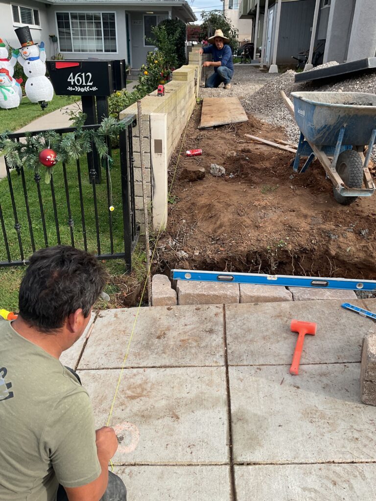 Crew members installing concrete pavers at a front entry/driveway approach next to a low concrete block retaining wall....