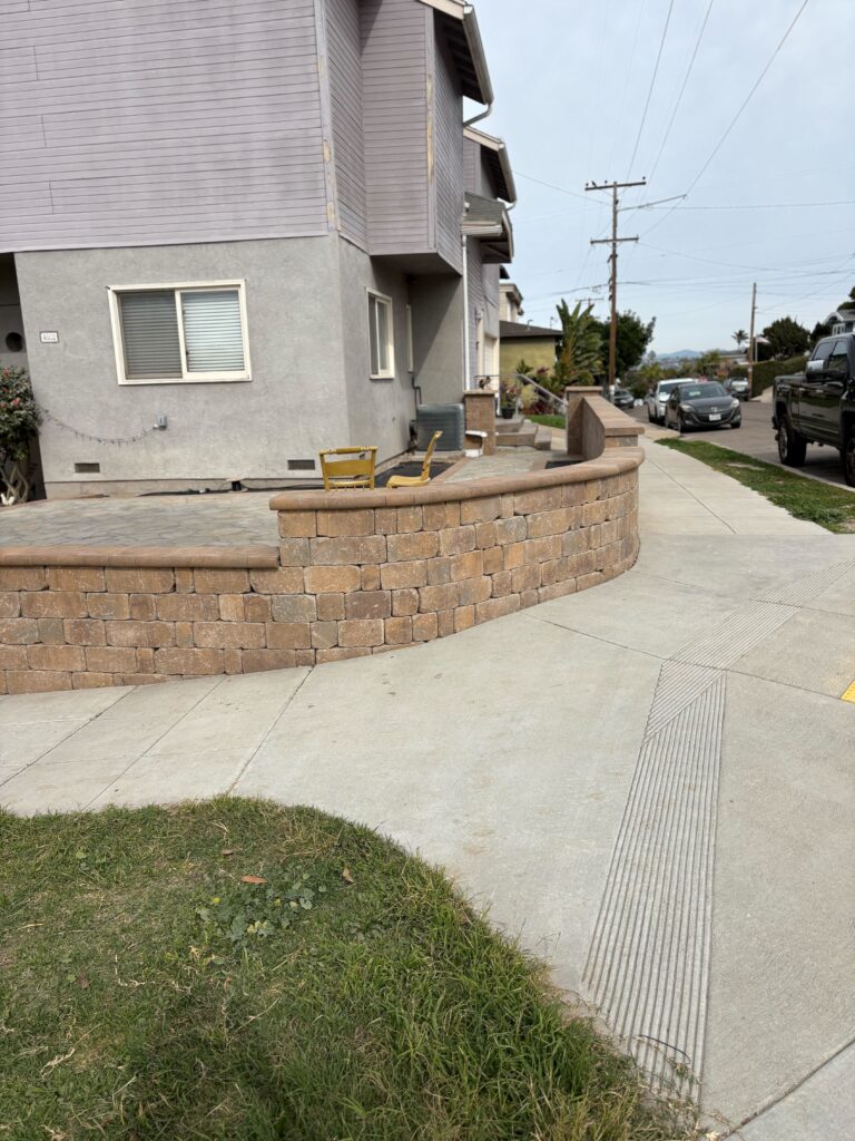 Finished segmental retaining wall with capstone borders a recently installed paver patio adjacent to a concrete public...