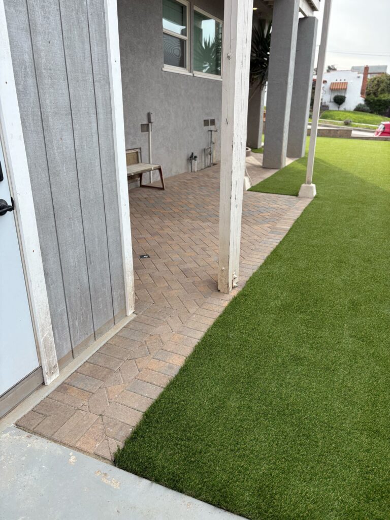 Completed backyard area showing interlocking pavers forming a curved walkway/patio under a covered patio with structural...