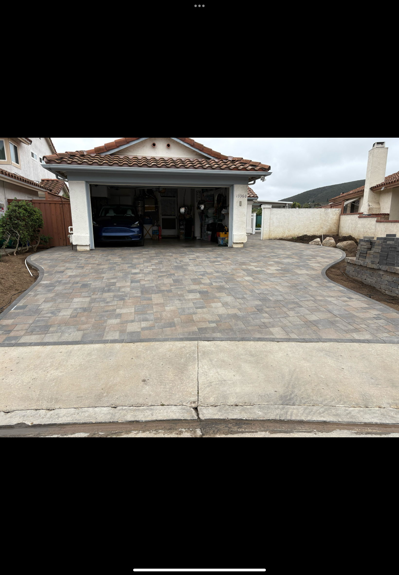 Finished interlocking concrete paver driveway with a contrasting soldier-course border leading to an attached garage. Low...