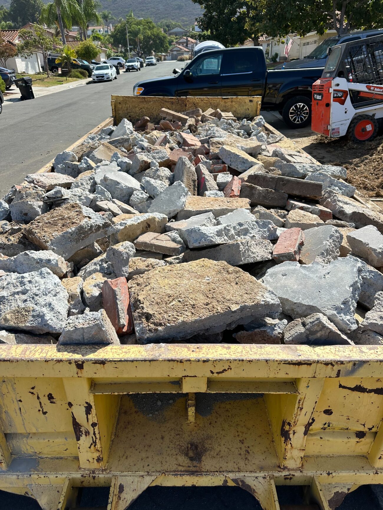 Roll-off dumpster loaded with demolition debris including broken concrete slabs and brick fragments at a residential...