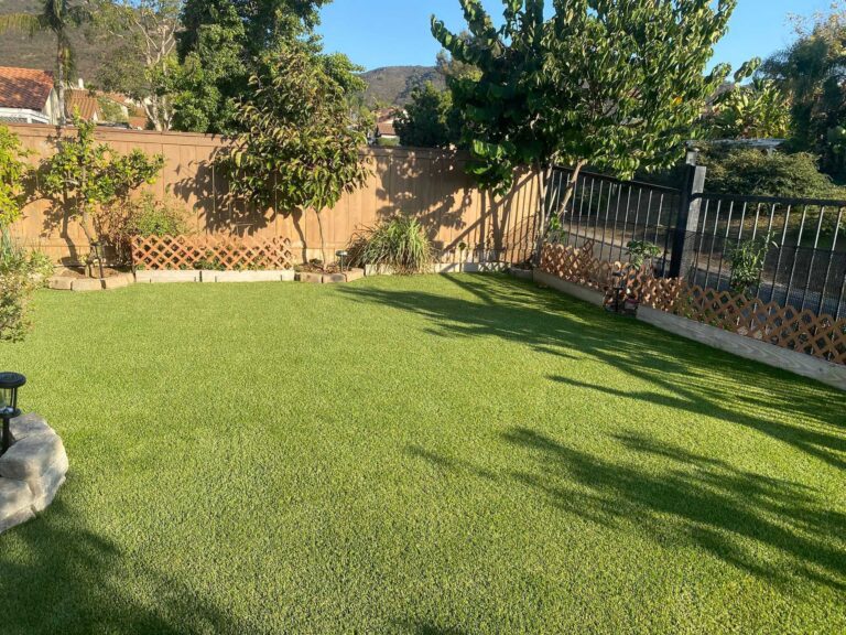 Residential backyard showing a completed artificial turf installation with clean, uniform turf field and defined...