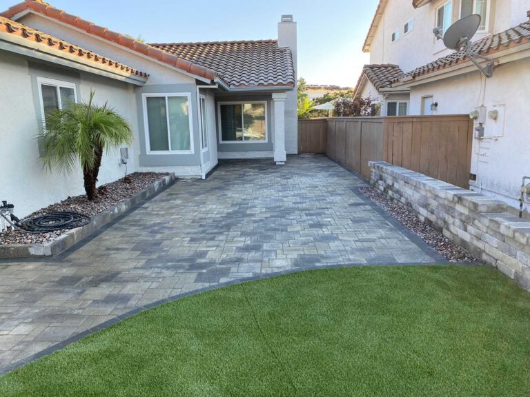 Finished interlocking paver patio with a curved artificial turf area in a residential backyard. Segmental retaining wall...