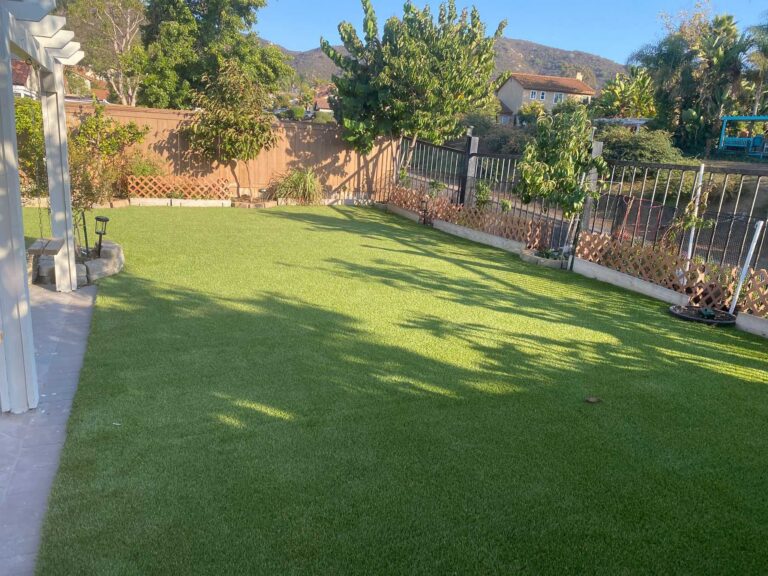 Finished residential backyard showing a full artificial turf installation with clean edges and smooth surface. Turf is...