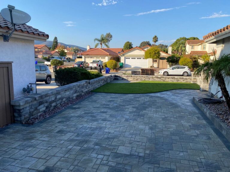 Finished interlocking paver driveway and adjoining patio with newly installed artificial turf and a low segmental stone...