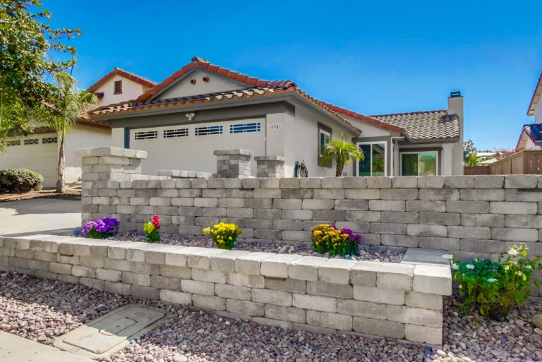 Tiered segmental retaining wall in Angelus Rustic Wall Stone with capped pilasters and flower pockets across the front-yard border.