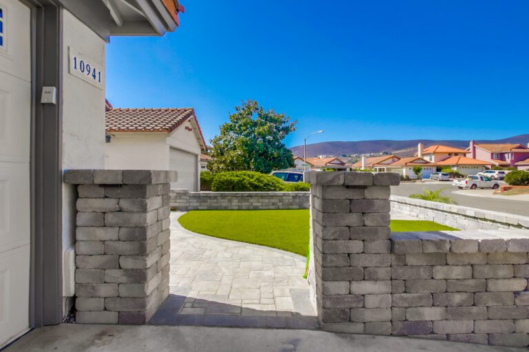 Capped stone pilasters at the entry frame the turf lawn, the paver walk, and the cul-de-sac and hills beyond.