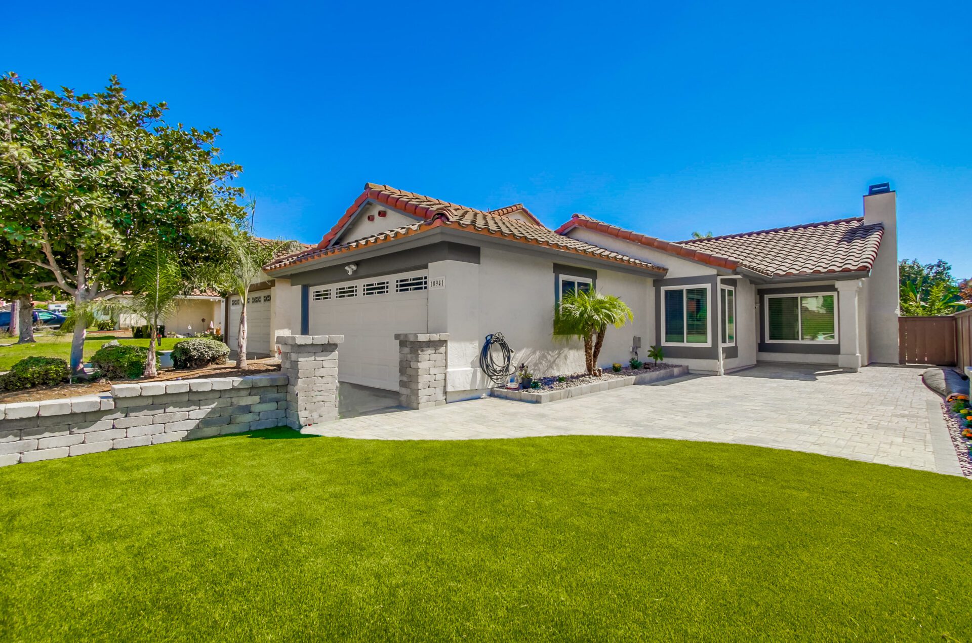 Finished Sabre Springs front yard with an Angelus paver driveway, a tiered segmental wall with capped pilasters, and an artificial-turf lawn.