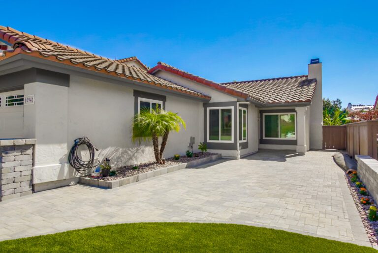 Angelus paver courtyard leading to the covered front entry, edged by a river-rock planting strip with a windmill palm.