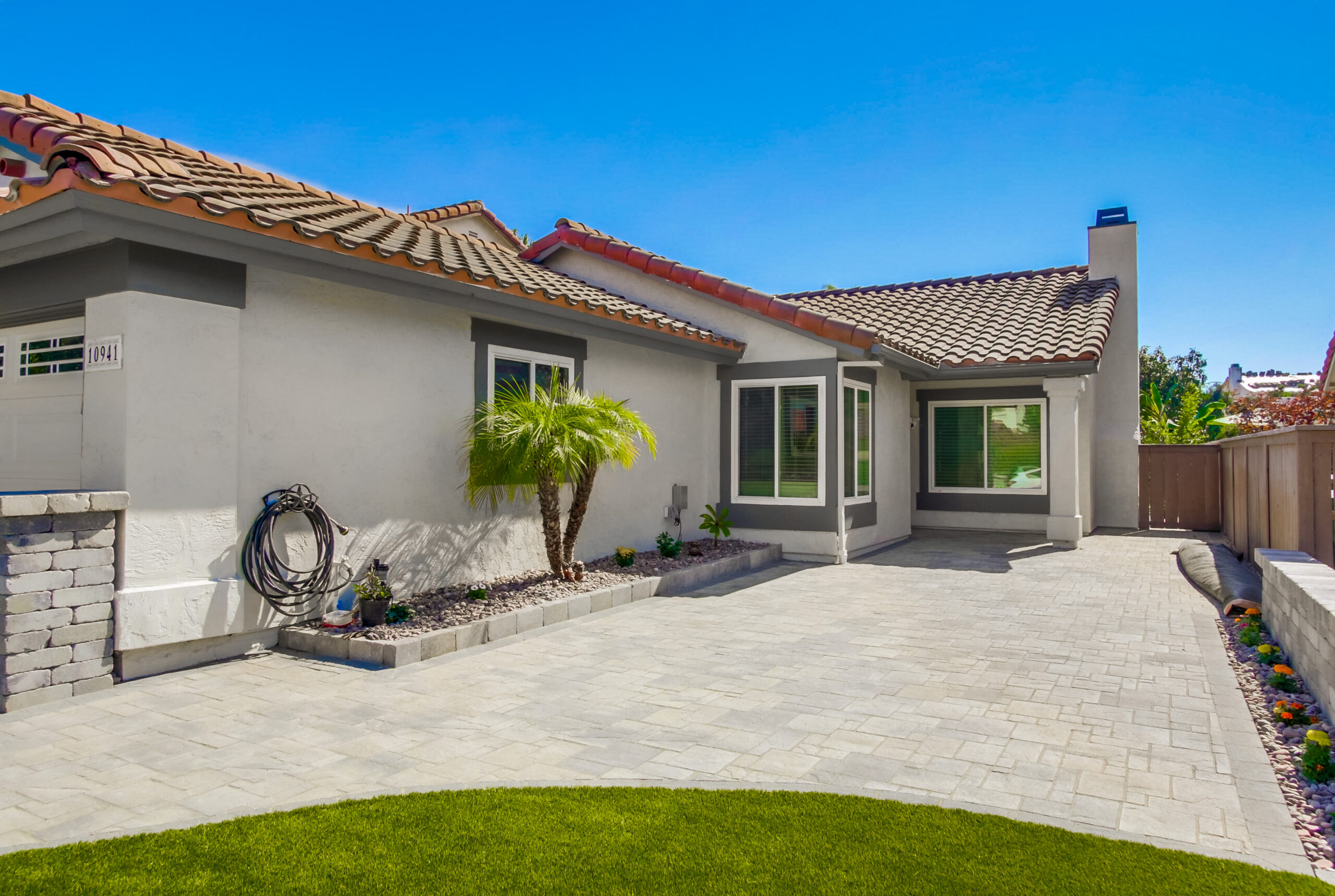 Angelus paver courtyard leading to the covered front entry, edged by a river-rock planting strip with a windmill palm.