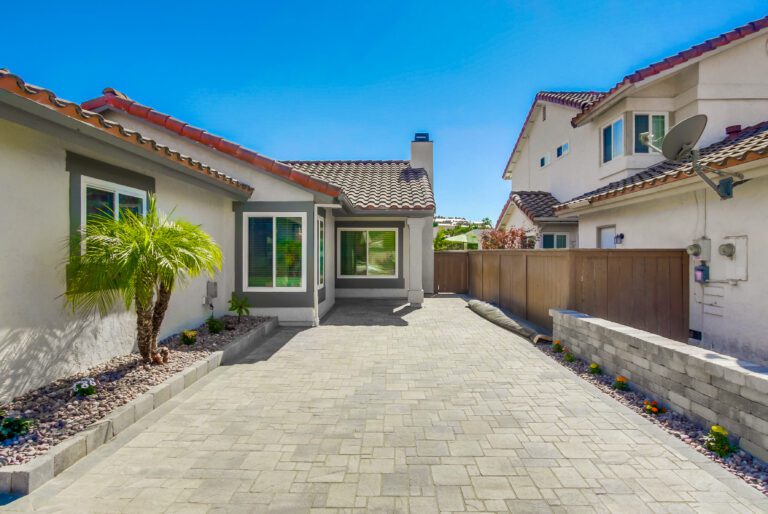 Side-yard Angelus paver walkway running alongside the house, bordered by river-rock drainage strips.