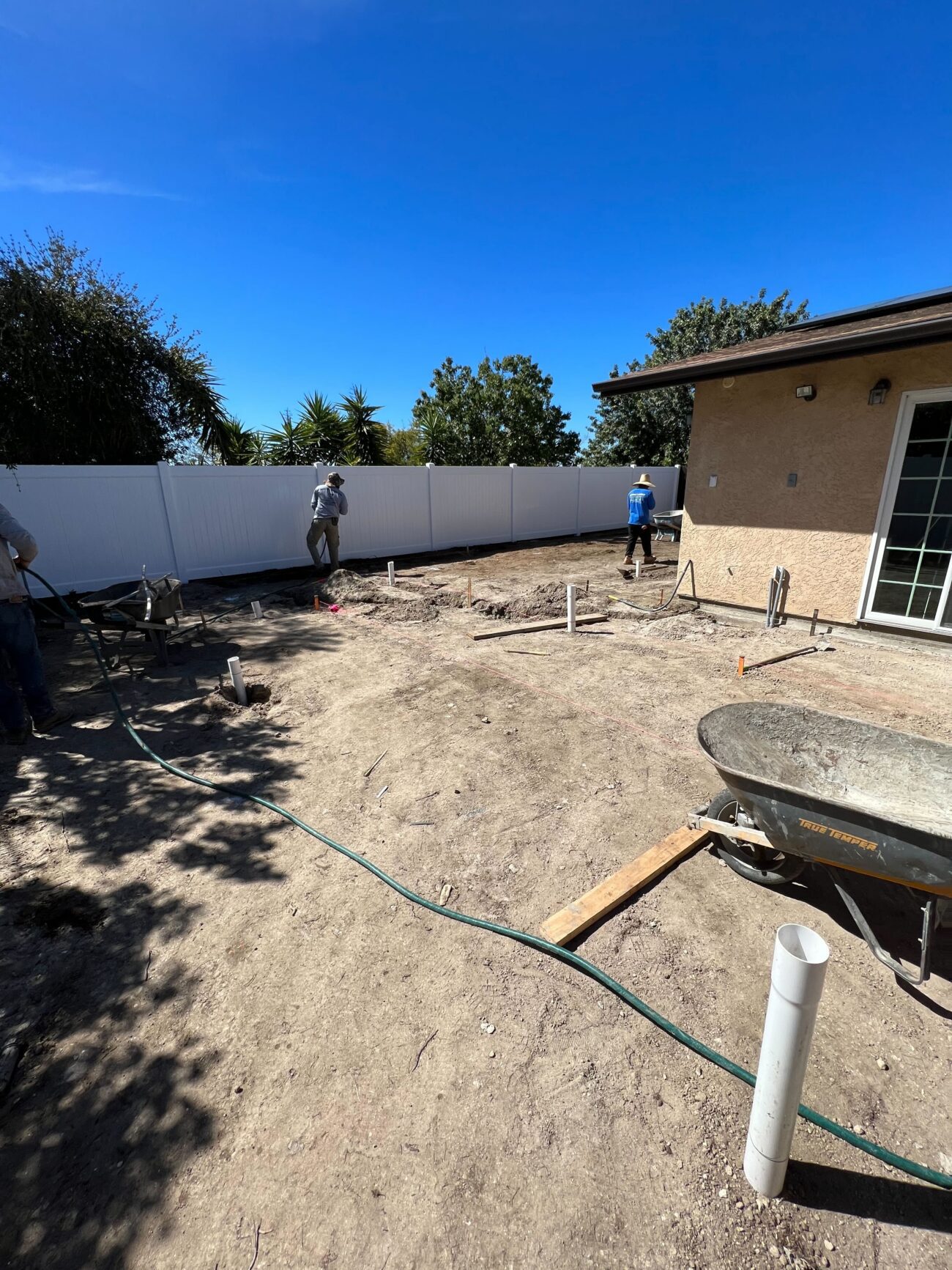 Backyard subgrade preparation for a future hardscape — exposed soil with workers leveling and preparing the area adjacent...