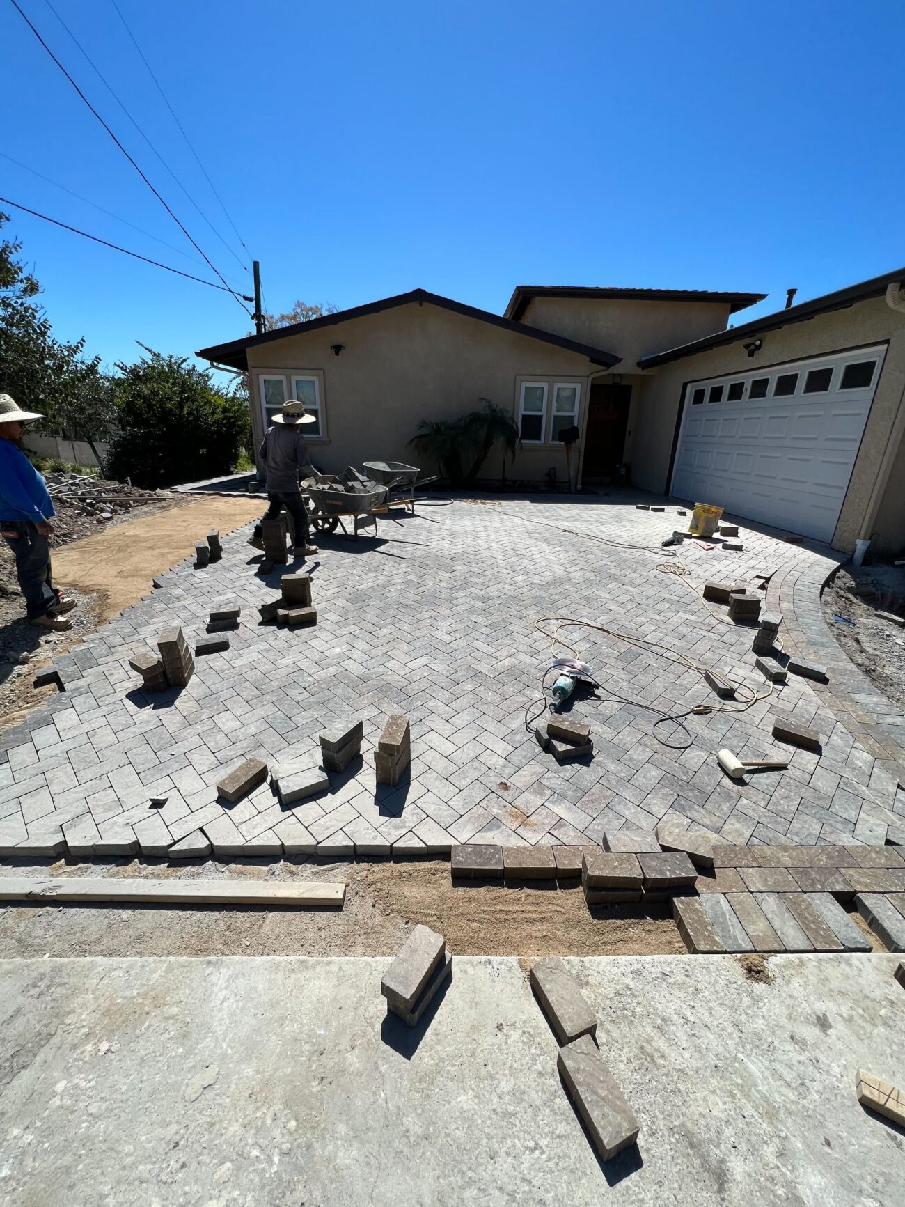 Residential driveway where interlocking pavers are being installed in a herringbone pattern; a sand base and edge...