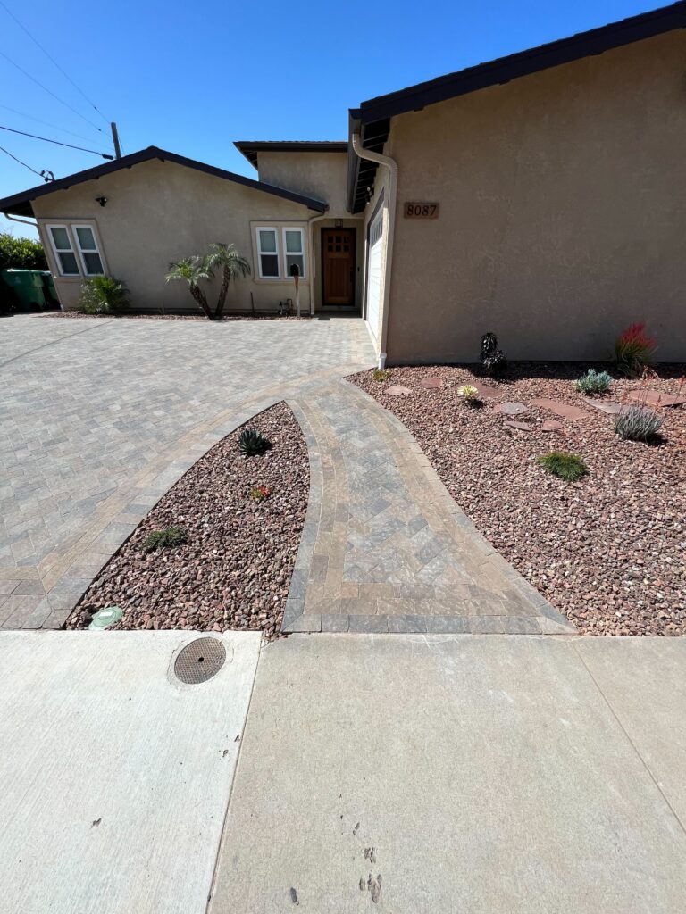 Front yard showing a completed interlocking paver driveway and a curved paver walkway leading to the home entry. Rock...