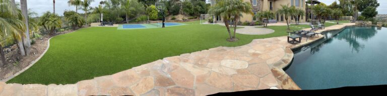Large residential backyard showing newly installed artificial turf adjacent to a freeform pool with flagstone patio and...