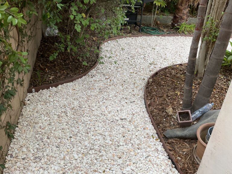 Finished narrow side-yard walkway surfaced with decorative white crushed stone/shell and a continuous metal edge...