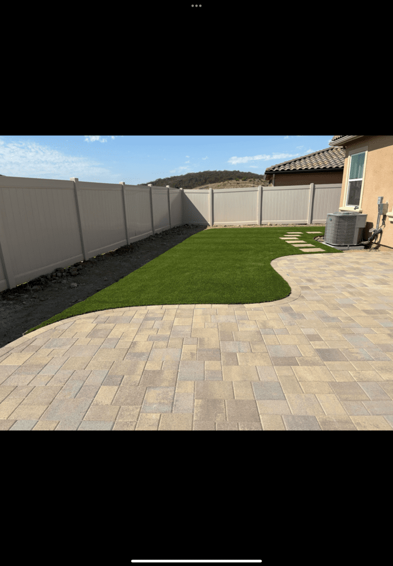 Finished interlocking paver patio transitions into a newly installed artificial turf lawn with a smooth curved edge. San Marcos project by Install It Direct.