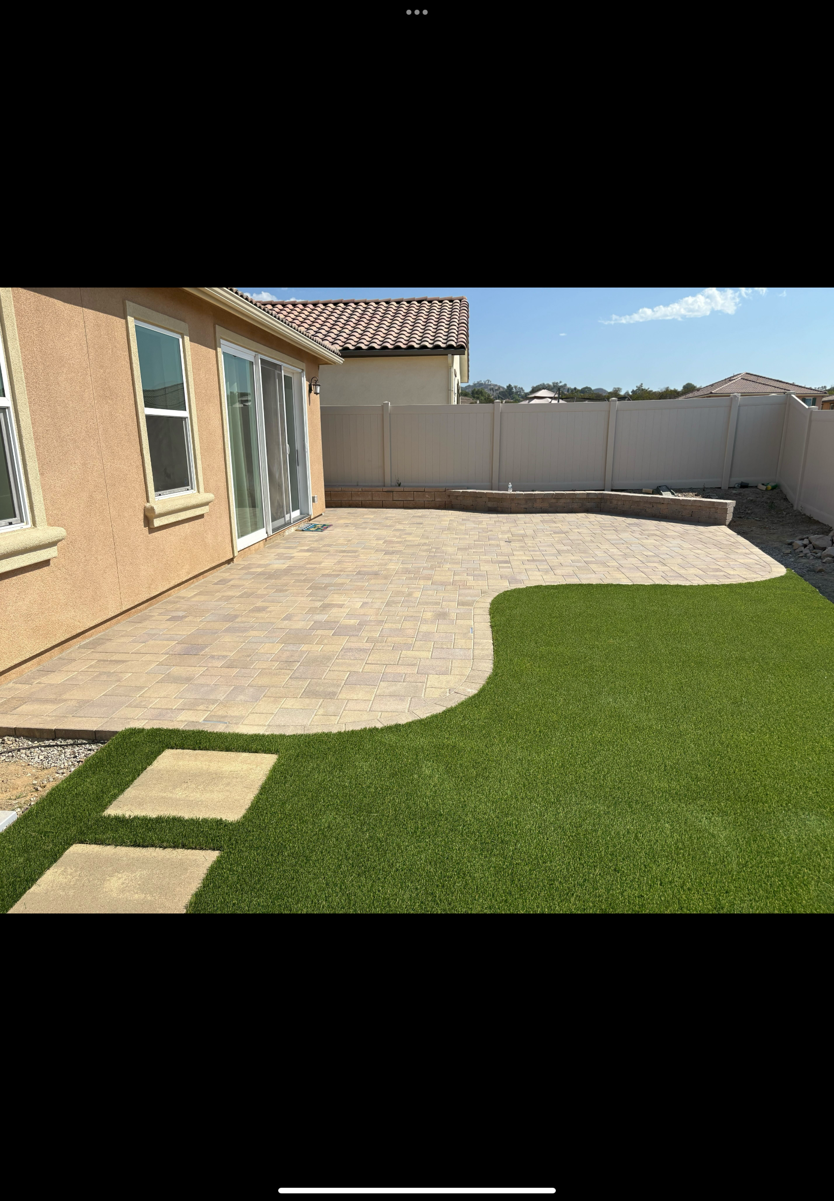 Newly installed interlocking paver patio with clean swept joints abutting a neatly trimmed artificial turf lawn and stepping stones. San Marcos project by Install It Direct.