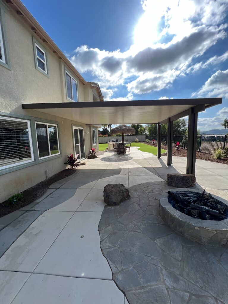 Completed backyard outdoor living area showing a covered patio with an aluminum patio cover, concrete walkways and...