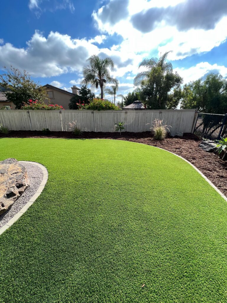 Residential backyard showing newly installed artificial turf with a smooth curved edge transitioning to a mulch planting...