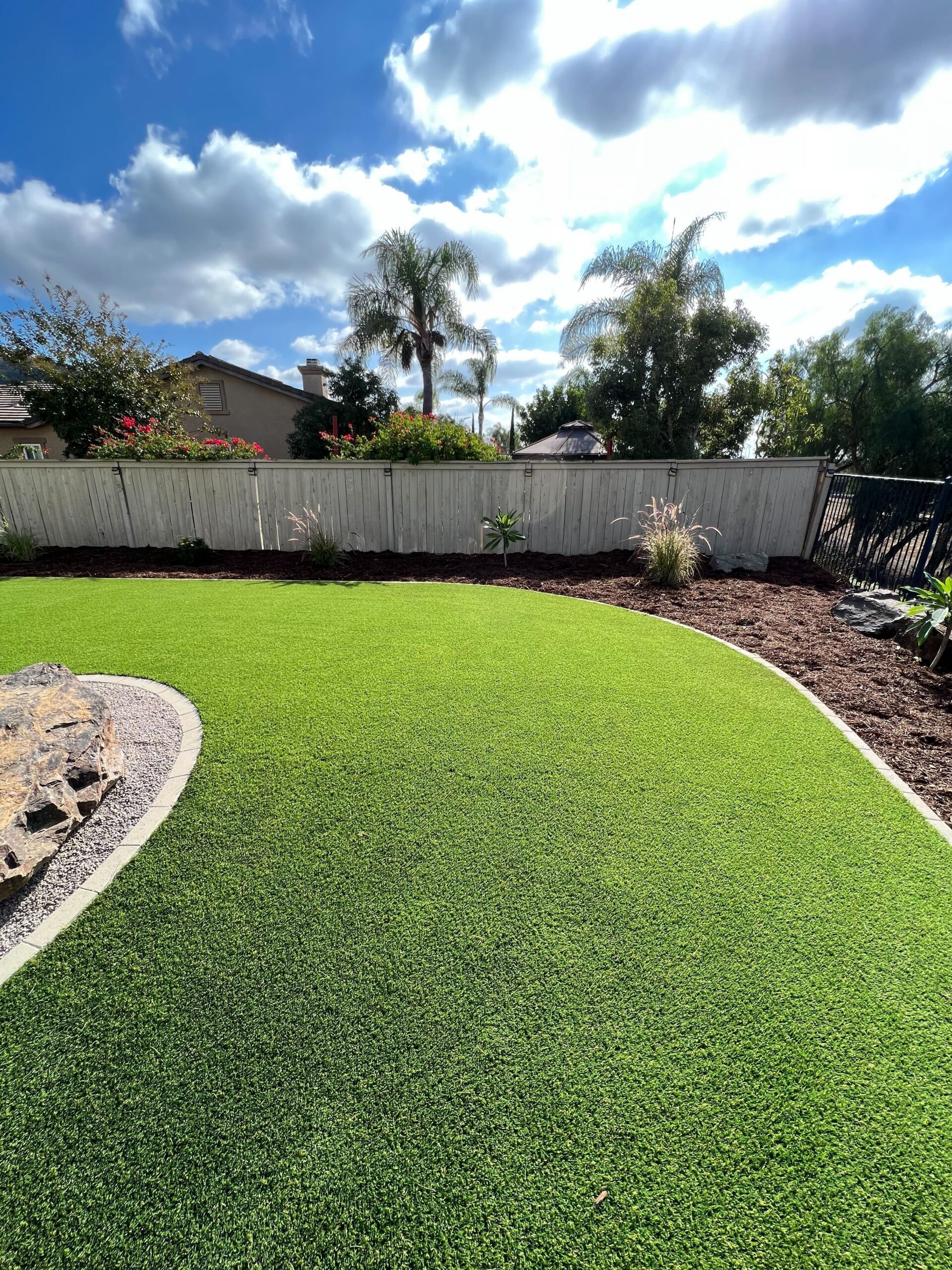 Residential backyard showing newly installed artificial turf with a smooth curved edge transitioning to a mulch planting...