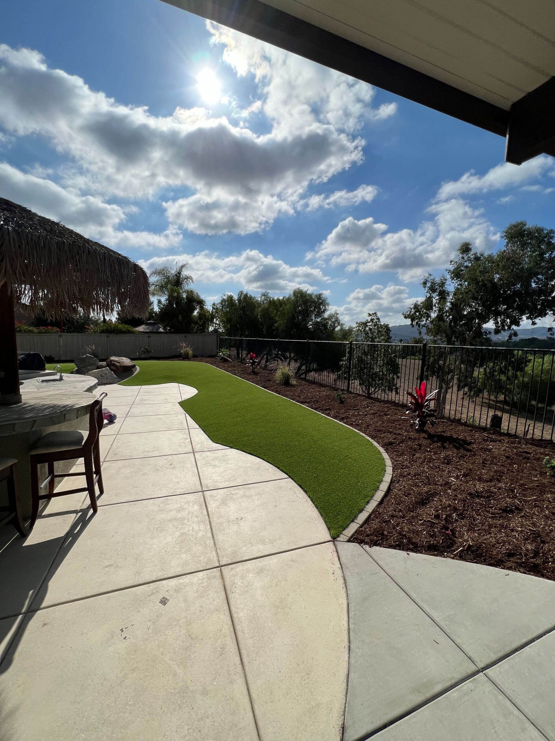 Residential backyard showing a recently finished curved concrete patio and adjacent artificial turf lawn with a mulch...