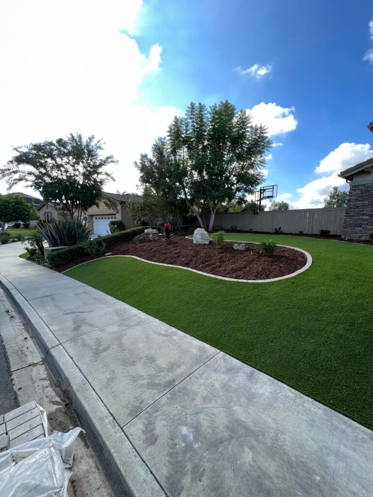 Residential front yard showing newly installed artificial turf with a smooth curved concrete curb edging separating a...