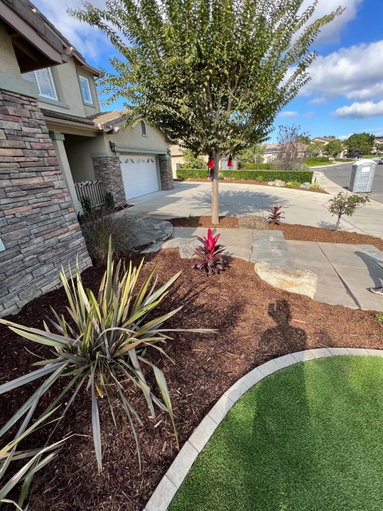Front yard of a residential project showing installed artificial turf with a curved concrete edge, adjacent paver/stone...