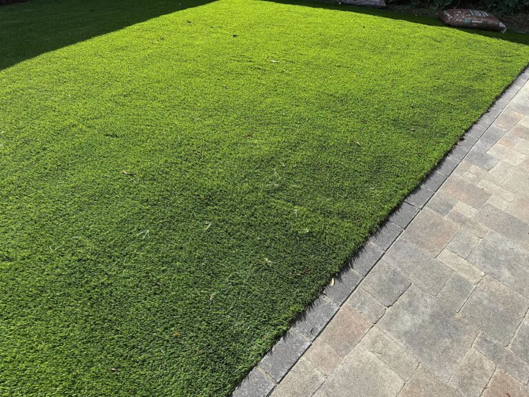 New artificial turf field installed directly adjacent to an interlocking paver patio. Clean edge transition between turf...
