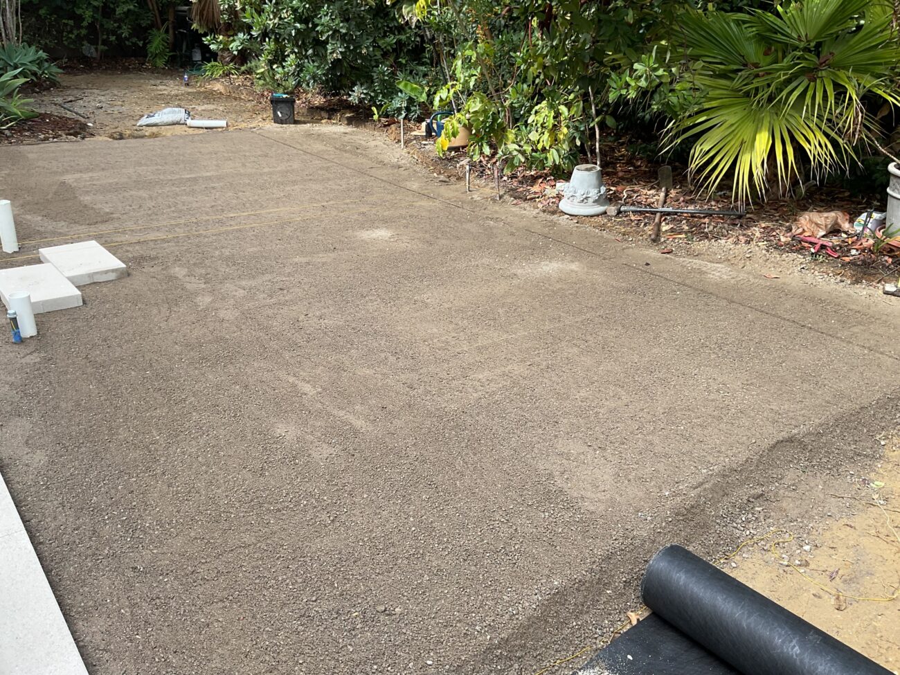 Compacted aggregate subbase prepared across a backyard area with visible compaction lines and a black geotextile/turf underlayment roll at the near edge. San Diego project by Install It Direct.