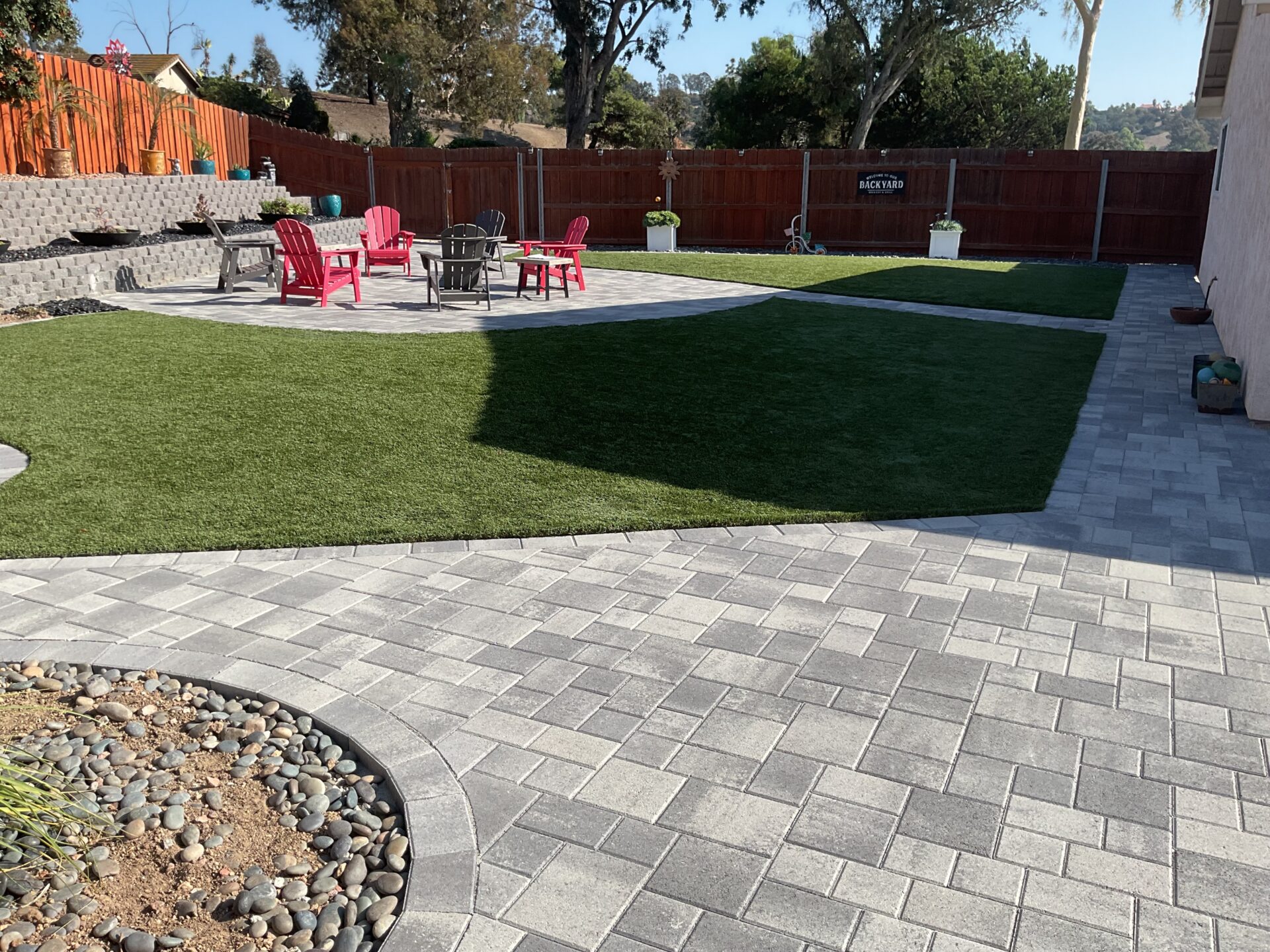 Finished backyard showing new interlocking paver patio and walkway surrounding an installed artificial turf lawn. San Diego project by Install It Direct.