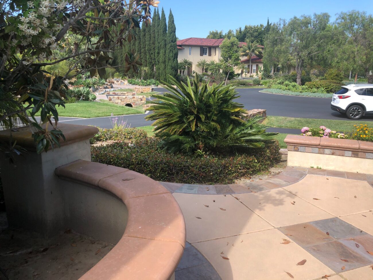 Residential front entry showing a finished paver patio and curved seat wall with capstone surrounding a planted bed with...