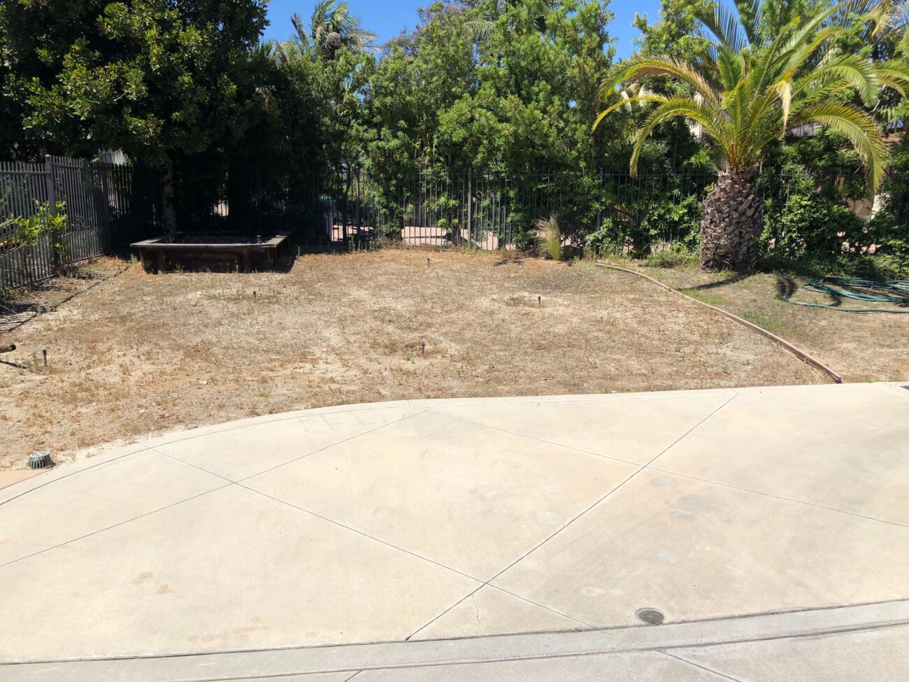 Foreground shows an existing concrete patio with control joints, adjacent to a large brown/dry turf and bare dirt area...