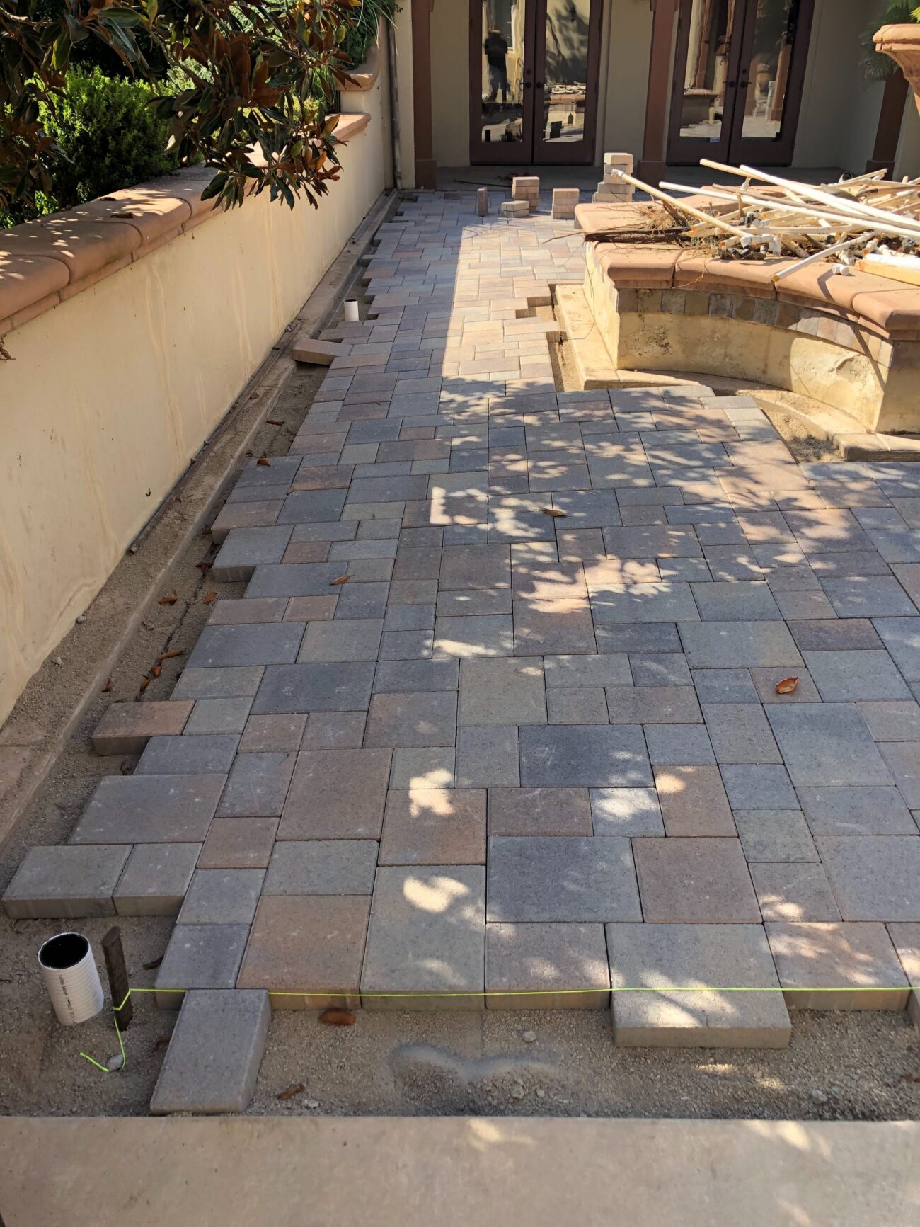 Backyard paver patio installation in progress showing interlocking pavers laid on a compacted sand/base with unfilled...
