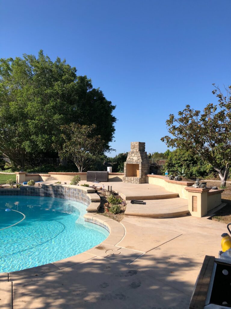 Finished residential pool deck and patio area featuring a curved concrete pool deck with integrated coping, curved steps,...