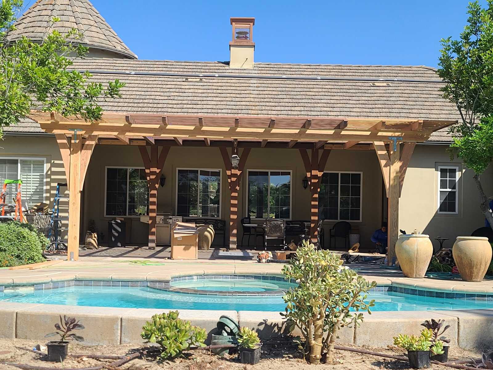 Backyard shows a completed pool deck and adjoining patio beneath an attached timber pergola. Integrated raised spa with...
