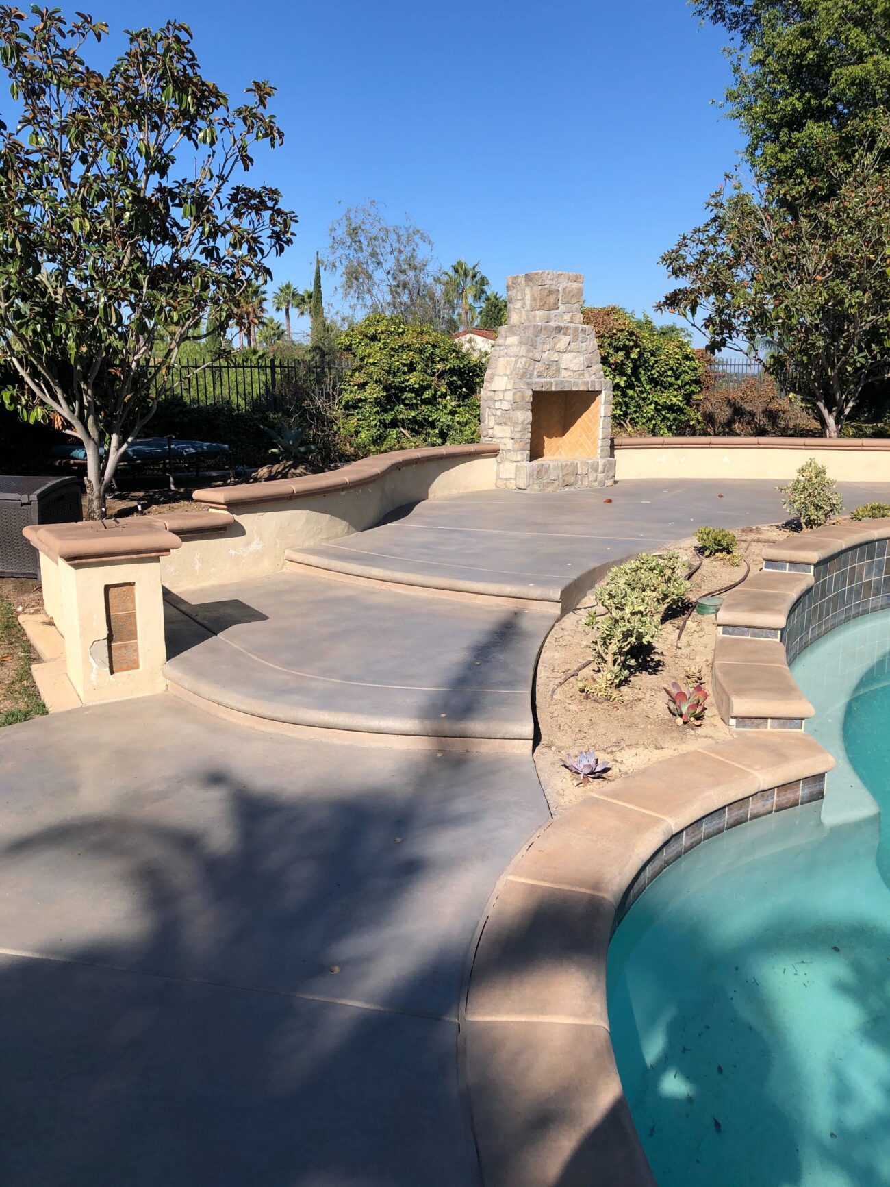 Residential backyard shows a finished stamped/sealed concrete pool deck and curved patio with integrated seat walls and a...