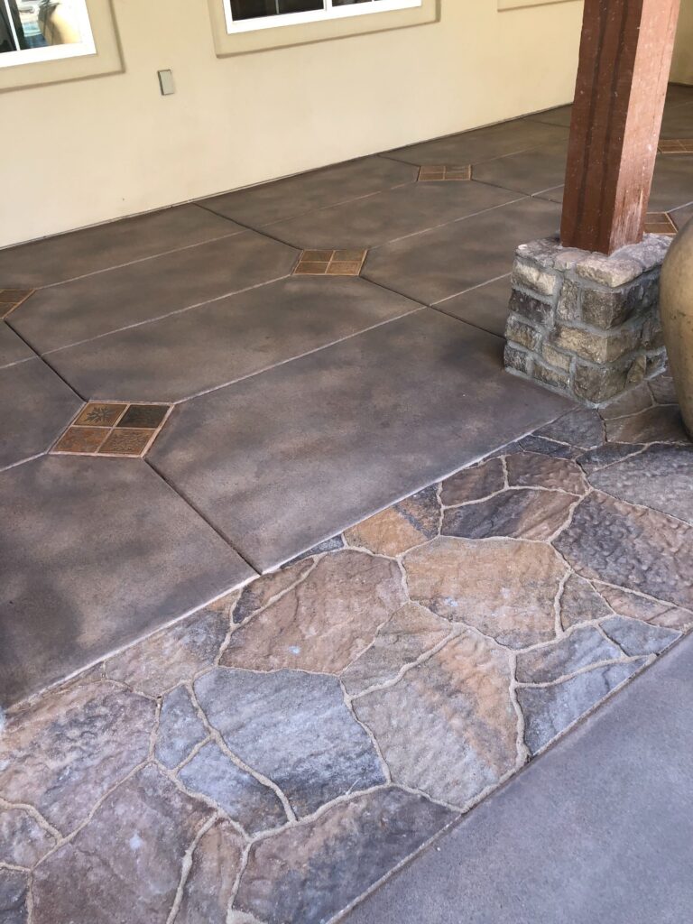 Stamped and stained concrete patio with a contrasting flagstone-patterned band and decorative square tile insets. A...