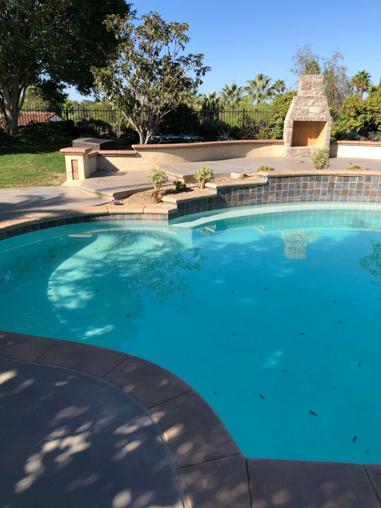 Completed residential pool deck and surrounding patio showing a concrete deck with tile waterline and stone-faced outdoor...