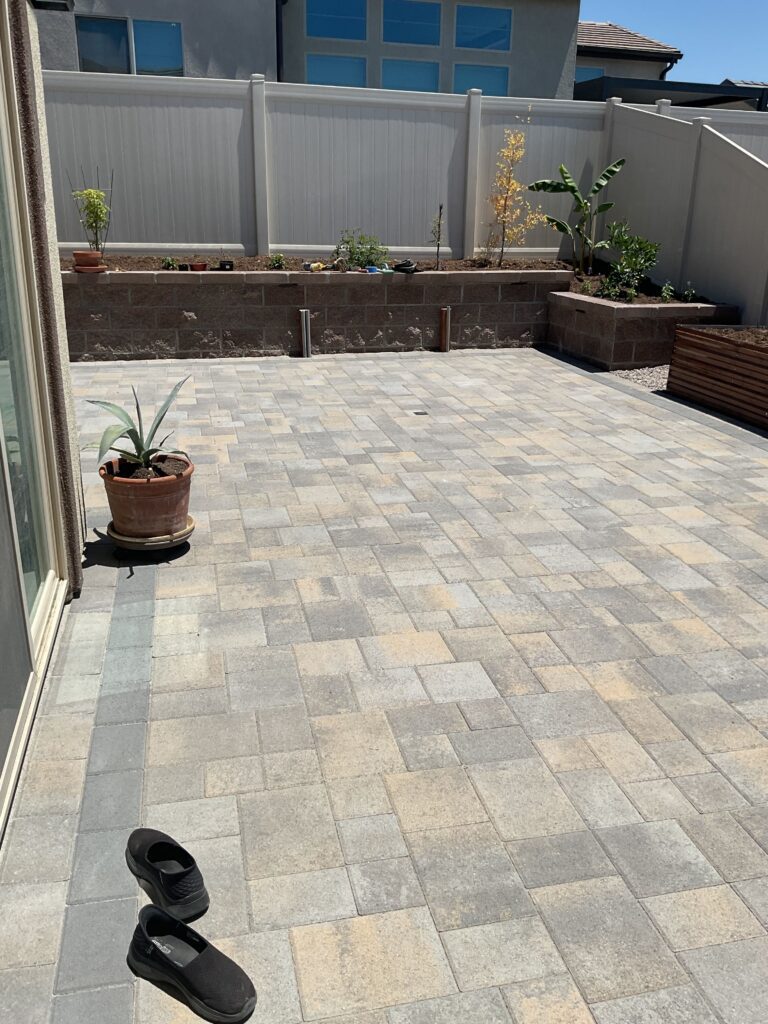 Finished residential paver patio using mixed-size interlocking concrete pavers laid in an ashlar-style pattern. A low...