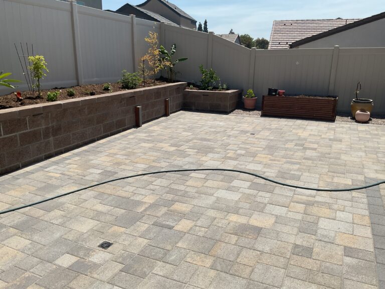 Interlocking paver patio installed with a segmental retaining wall planter running along a vinyl fence. Integrated...