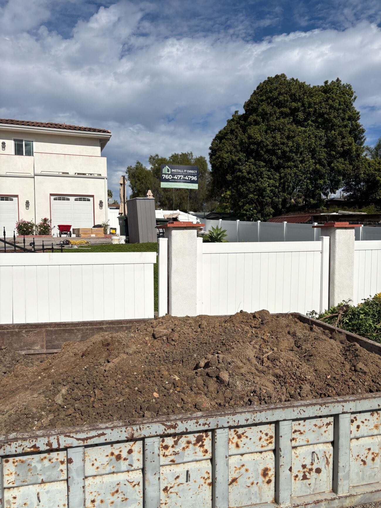 Roll-off container loaded with excavated soil in the side yard on demo day at a Vista backyard build. Install It Direct project.