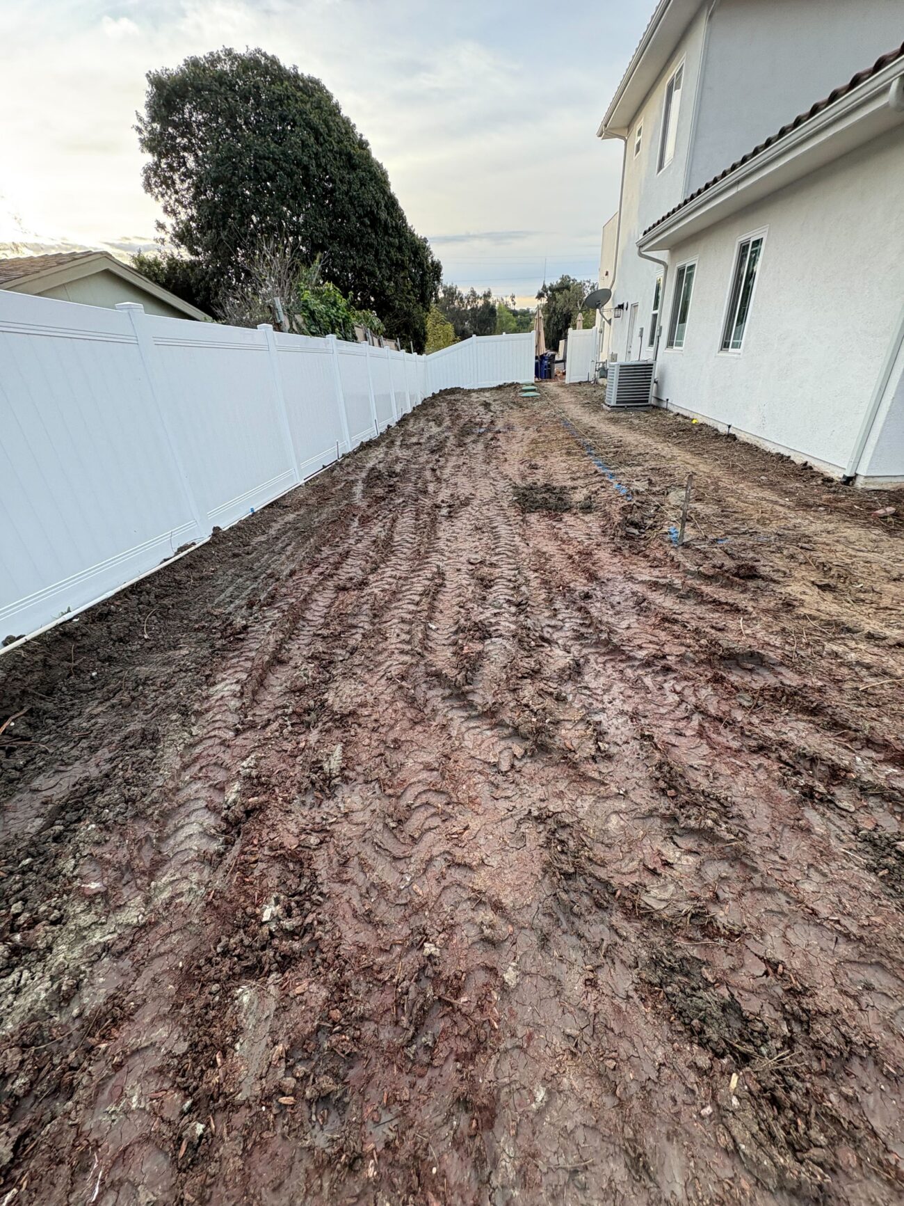 Long narrow side-yard subgrade after excavation, with rough-graded clay-heavy soil staged for base prep in Vista, CA. Install It Direct project.