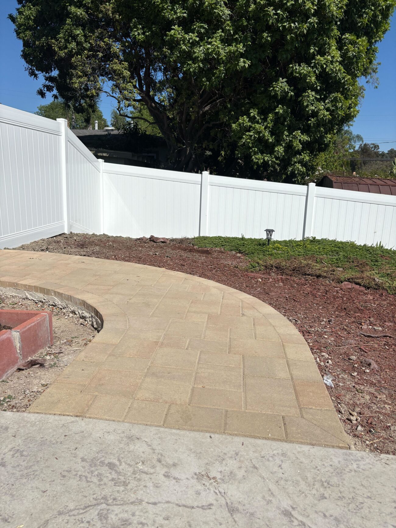 Curved interlocking concrete paver walkway and patio installed adjacent to the white vinyl fence in Vista, CA. Install It Direct project.