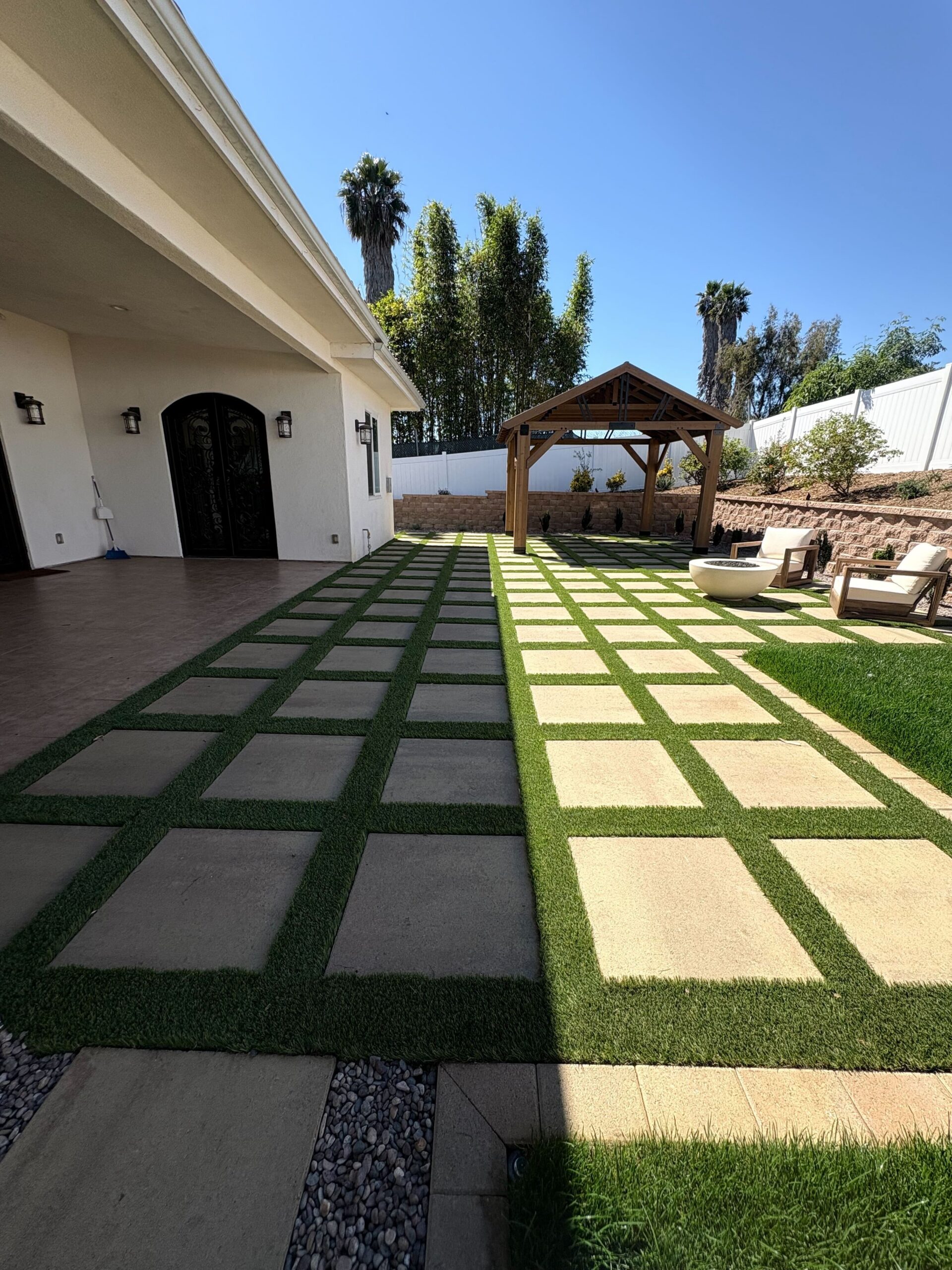 Paver-and-turf checkerboard patio with timber pergola, fire feature seating, and segmental retaining wall in Vista, CA. Install It Direct project.