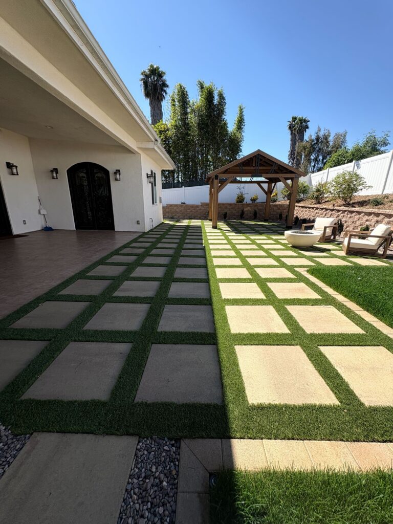 Paver-and-turf checkerboard patio with timber pergola, fire feature seating, and segmental retaining wall in Vista, CA. Install It Direct project.