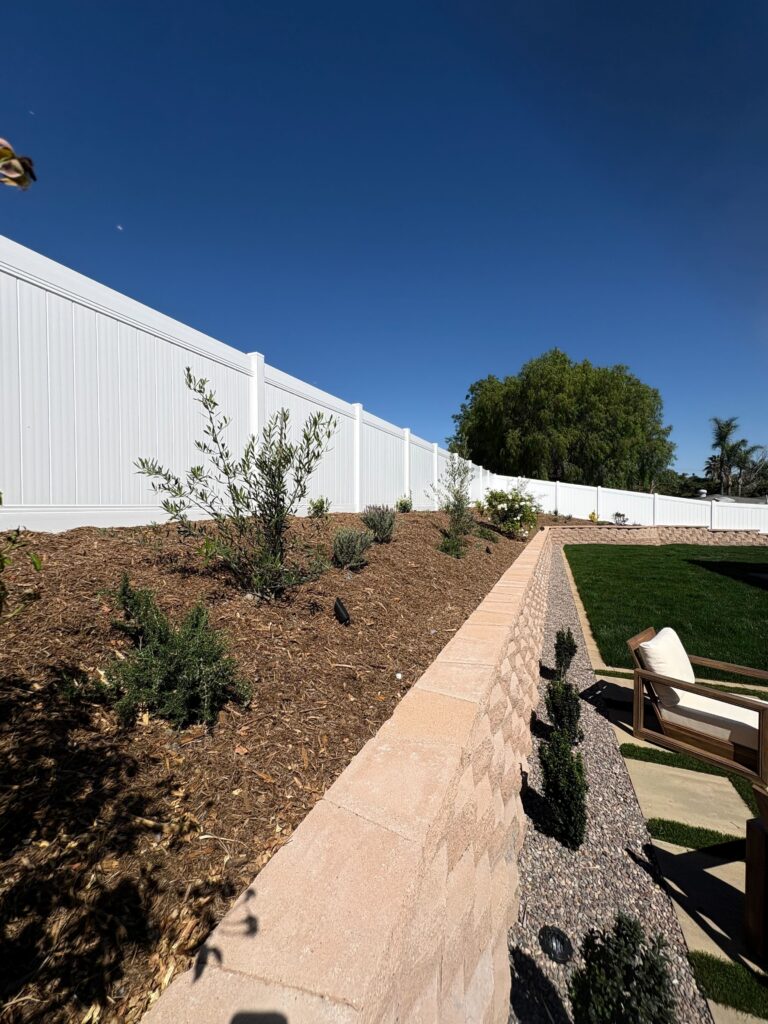 Capped segmental retaining wall above artificial turf lawn with mulched planting slope and landscape lighting in Vista, CA. Install It Direct project.