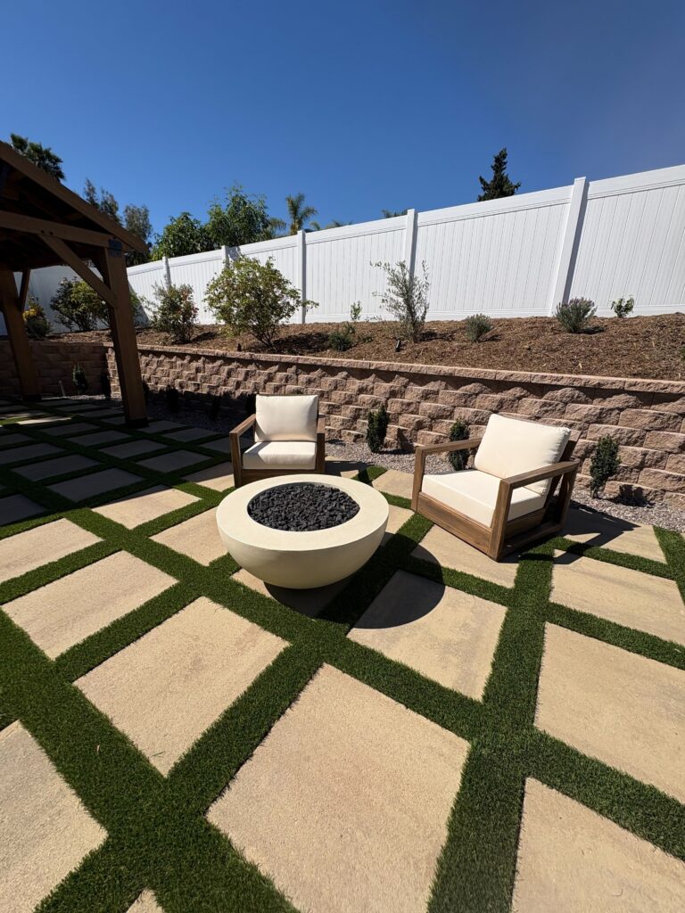 Round fire feature and seating on the paver grid with white vinyl fence above the segmental retaining wall in Vista, CA. Install It Direct project.